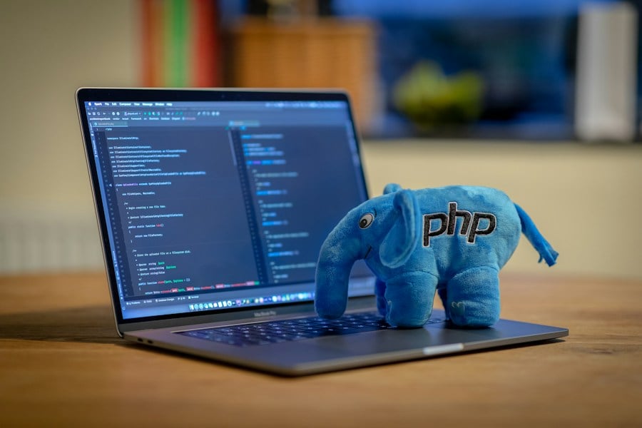 A blue PHP elephant plush toy on a laptop displaying PHP code in an IDE.