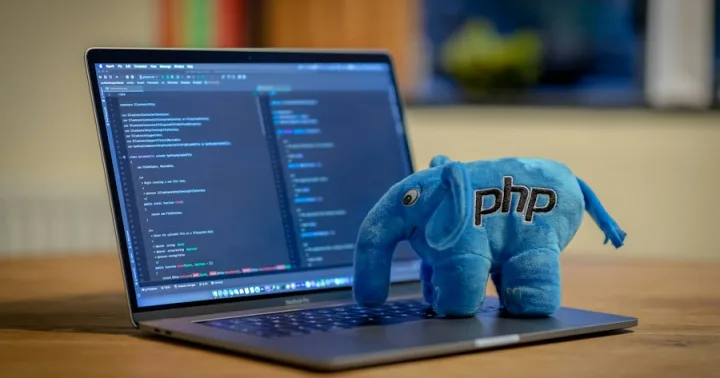 A blue PHP elephant plush toy on a laptop displaying PHP code in an IDE.